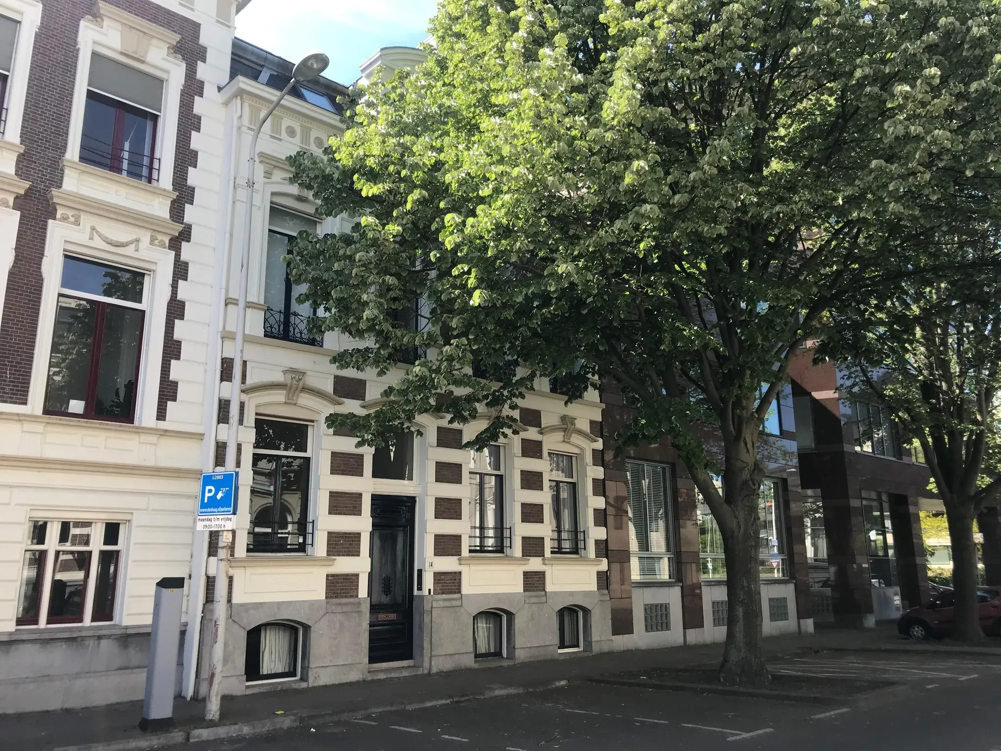 Voorgevel van een historisch pand aan de Burgemeester van Karnebeeklaan met een boom en parkeerplaatsen op de voorgrond.